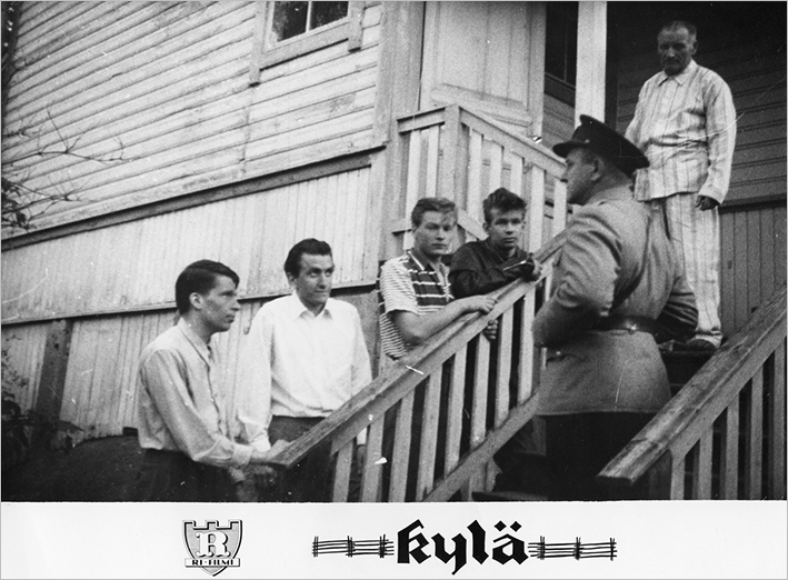 Mustavalkoinen valokuva talon ulkorappusista, joilla seisoo poliisi. Poliisia vastapäätä seisoo neljä henkilöä kuuntelemassa häntä. Portaiden yläpäässä seisoo vielä yksi henkilö.